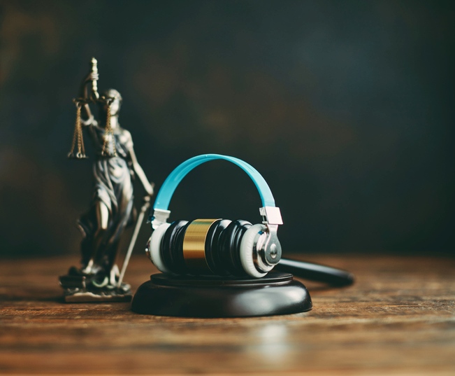 Lady Justice stands beside headphones perched atop a judge's gavel, symbolizing legal audio content. The image is featured within a content management system.